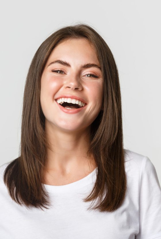 Close-up of happy brunette girl in white t-shirt laughing and smiling carefree at camera.